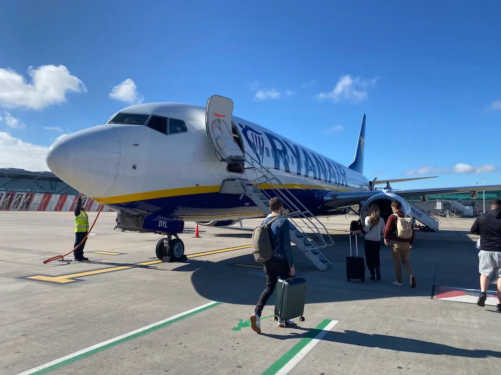 Passengers disembarking from a Ryanair plane under a cloudy sky.