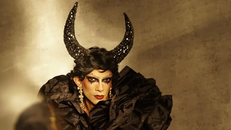 Drag artist Zeeshan Ali striking a pose while wearing a bold black wig with dramatic horns.