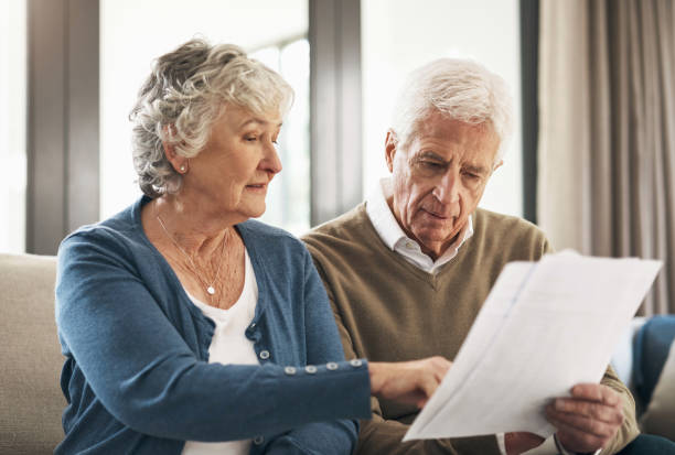 older couples reviewing household bills, highlighting financial pressures faced by older adults. | Wealth-Hoarding Boomers