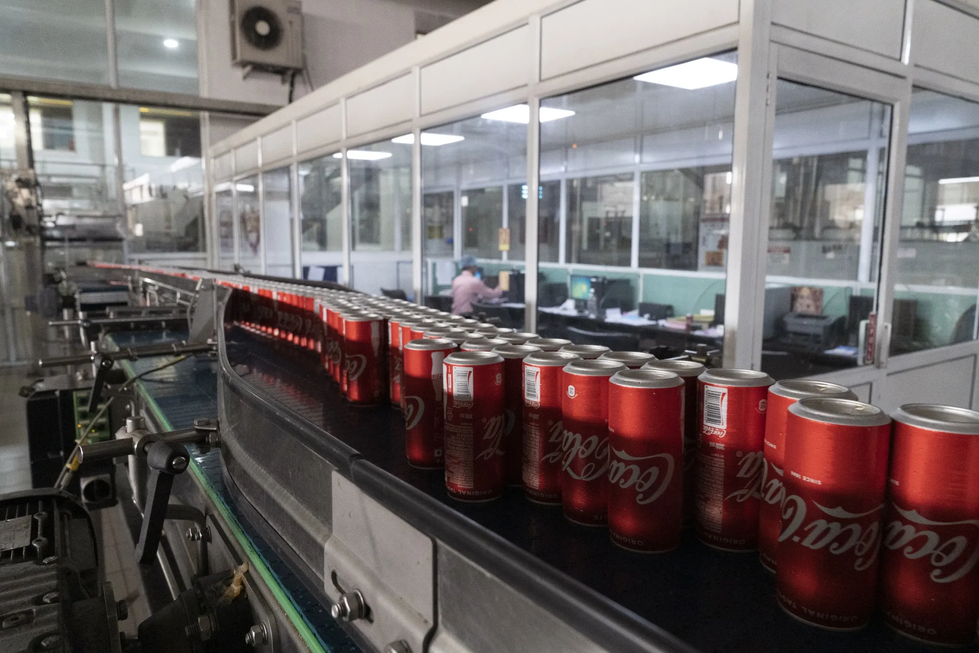 Cans of Coca-Cola moving along a conveyor belt at a bottling plant | metal tariffs